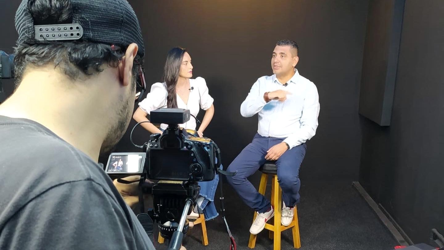 Grabación de una entrevista en estudio: camarógrafo en primer plano, presentadora y Alexánder Ricardo Andrade frente a cámara